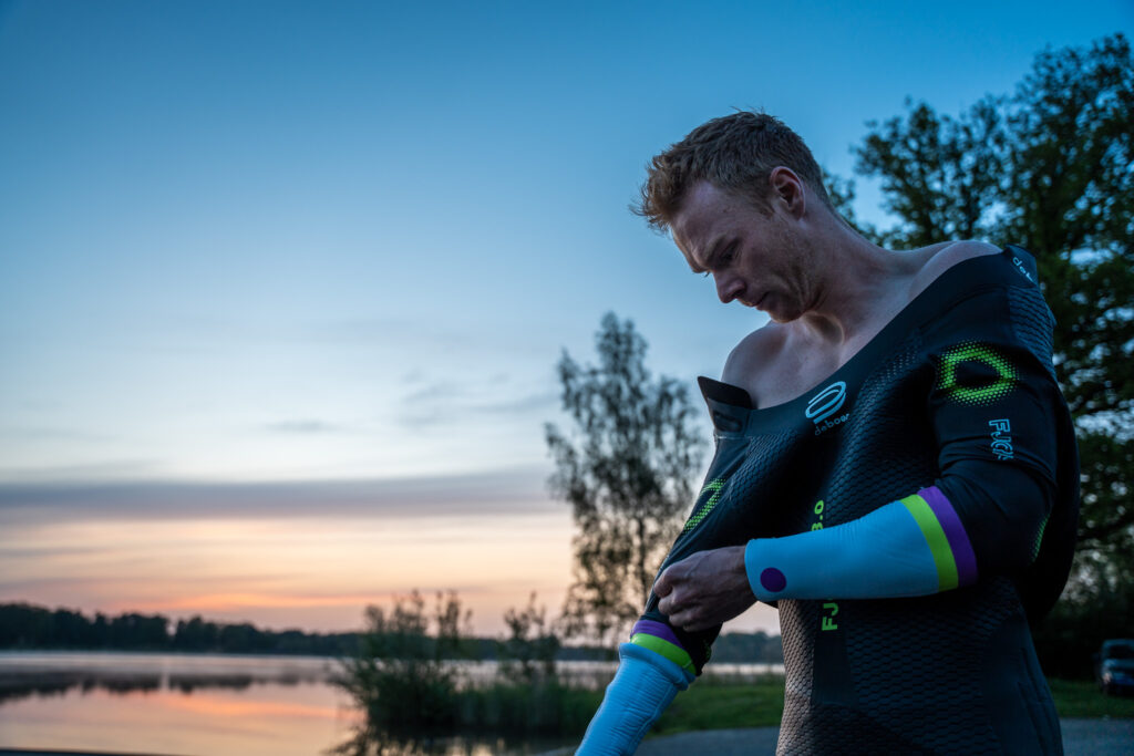 Triatleet Olaf van den Berg trekt zijn Fjord 3.0 wetsuit van DeBoer Wetsuits aan, vroeg in de ochtend tijdens blue hour. Photo by Ruben Huis in 't Veld