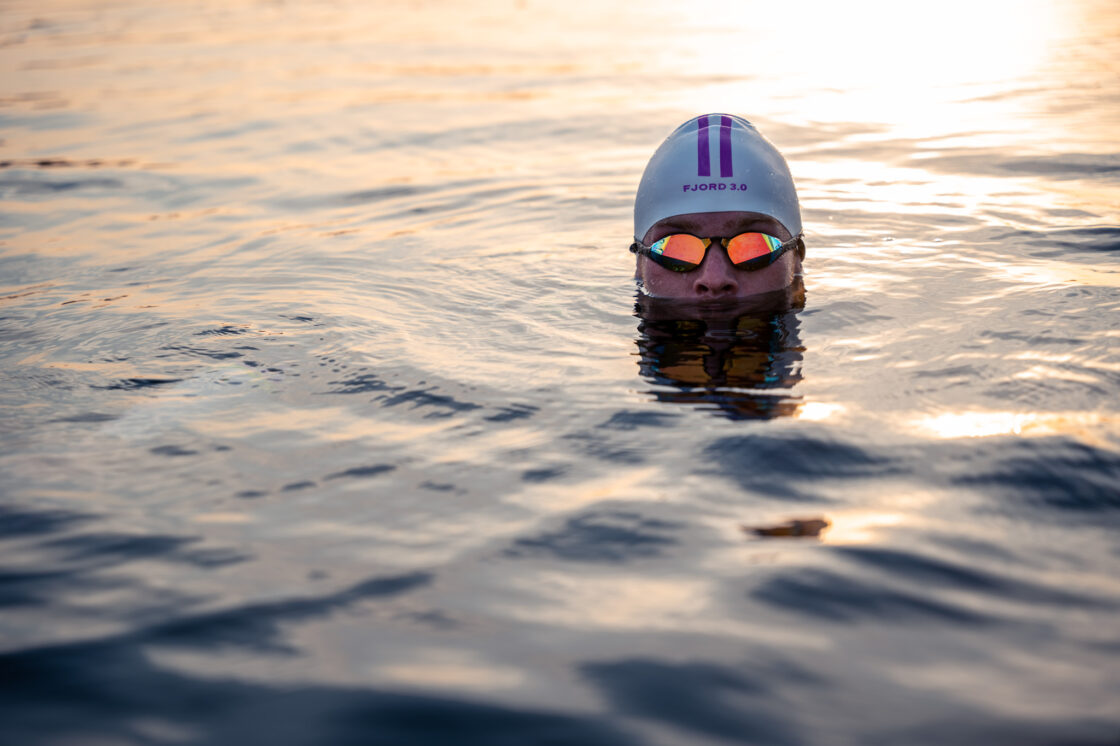 Triatleet Olaf van den Bergh ligt in het water met een badmuts van DeBoer Wetsuits, Fjord 3.0